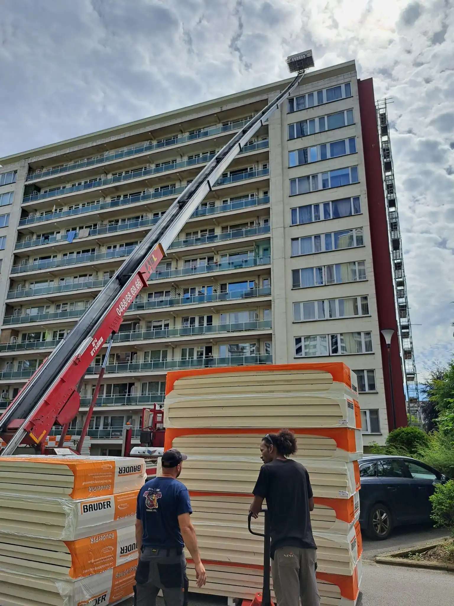 Des matériaux de rénovation de toitures sont transportés par une grue vers le toit d'un immeuble résidentiel.