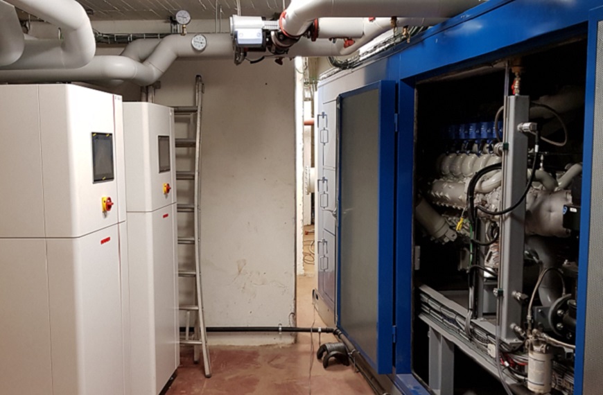 Salle technique avec des équipements industriels, comprenant des machines blanches et bleues, des tuyaux et une échelle contre le mur.