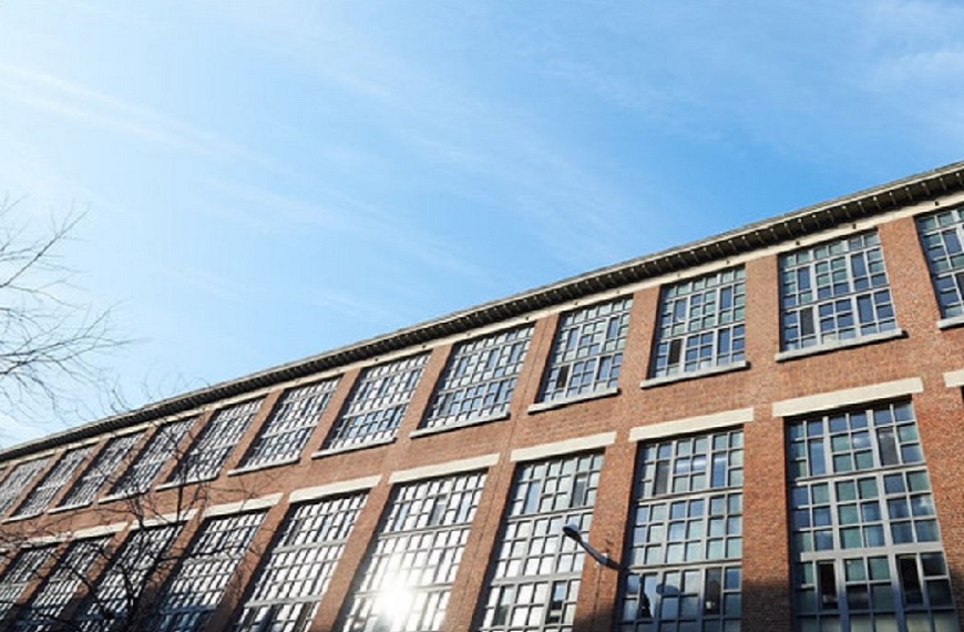 Bâtiment en briques rouges avec de grandes fenêtres, sous un ciel bleu clair, identifié comme 17-ACP-Pepibru.