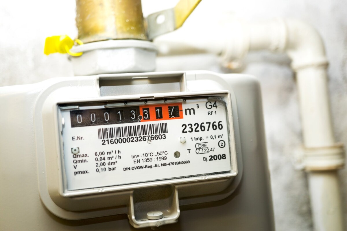 Compteur de gaz gris avec affichage numérique indiquant 1331, tuyau blanc connecté et étiquette jaune en arrière-plan.