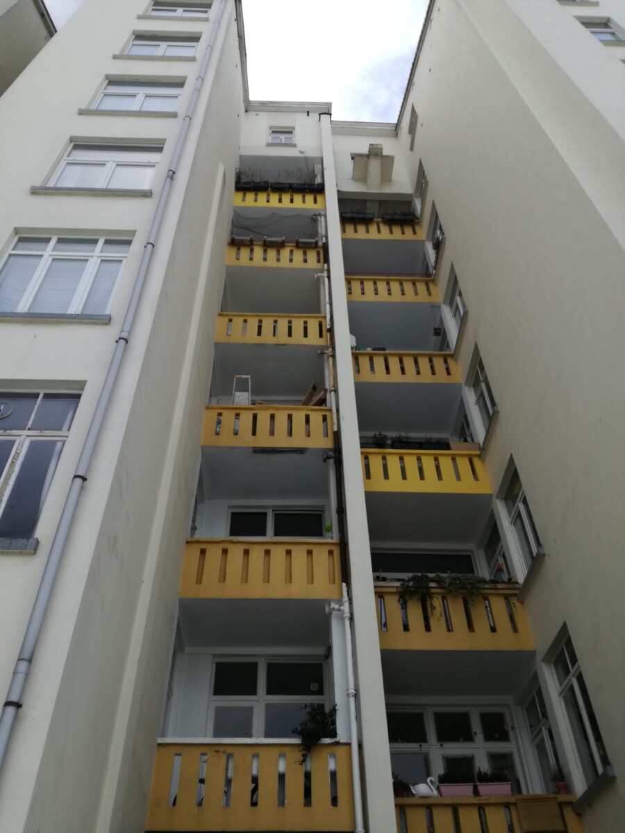 Immeuble résidentiel blanc avec balcons jaunes et fenêtres, vue en contre-plongée entre deux façades.