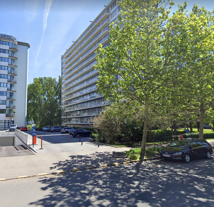 Immeuble résidentiel moderne Aurore 14 entouré d'arbres, avec un parking et des voitures stationnées à l'avant.