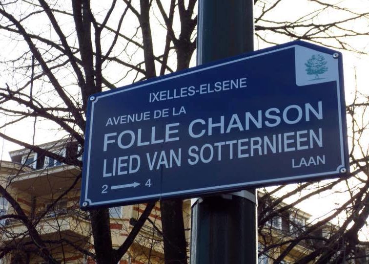 Panneau bleu indiquant l'avenue de la Folle Chanson à Ixelles, avec des arbres et un immeuble en arrière-plan.
