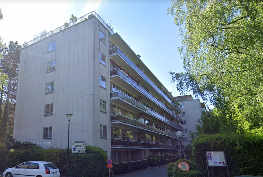 Immeuble résidentiel blanc de six étages à Steenvelt, avec balcons et arbres environnants, une voiture blanche stationnée devant.