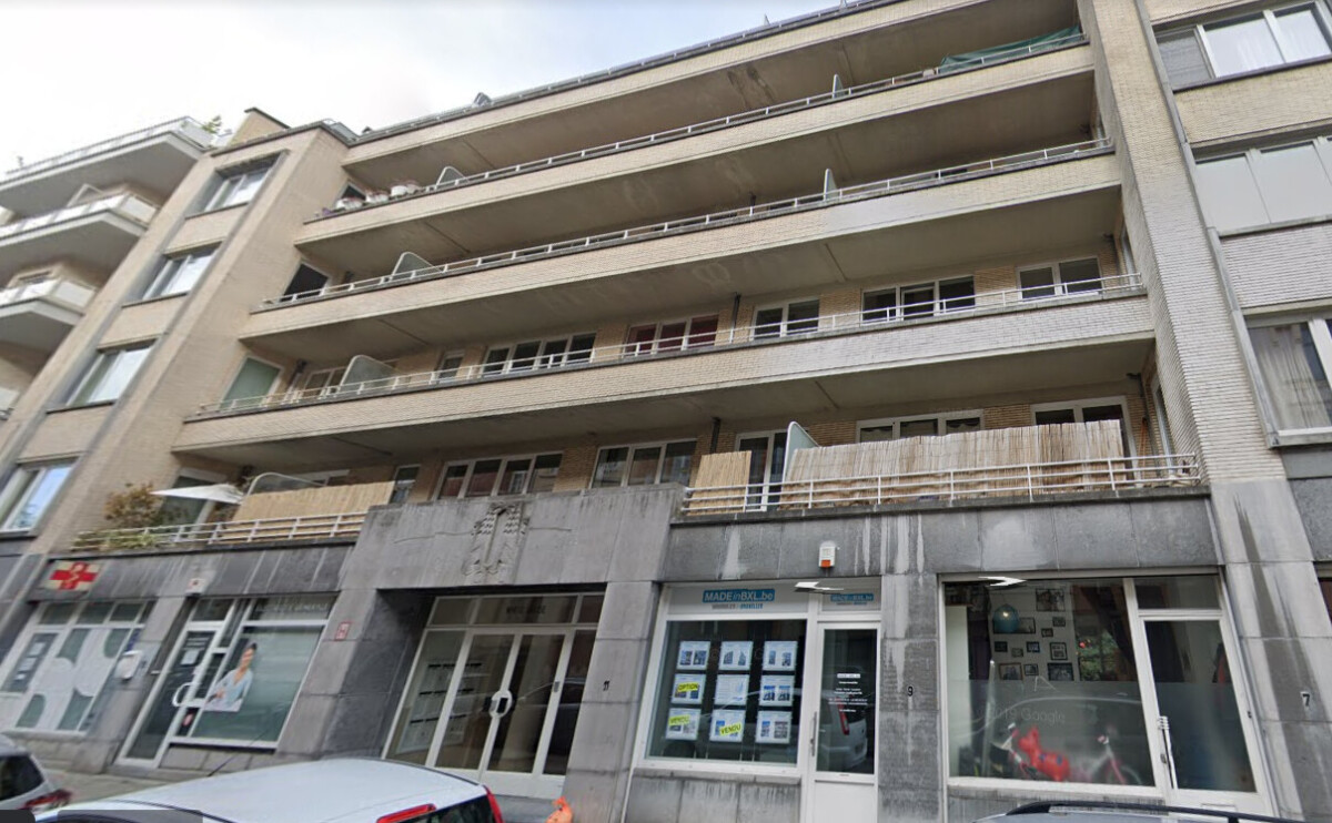 Un immeuble résidentiel beige à plusieurs étages avec des balcons et des vitrines commerciales au rez-de-chaussée.