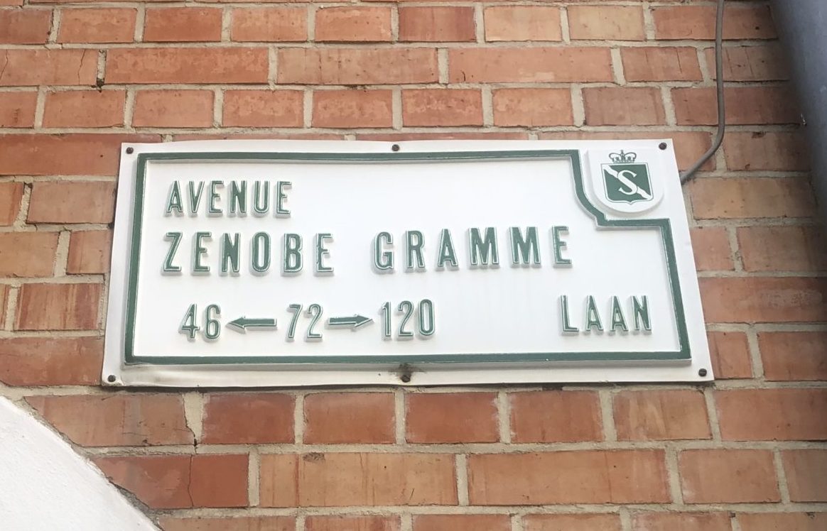 Plaque de rue blanche avec texte vert indiquant "Avenue Zenobe Gramme" sur fond de mur en briques rouges.