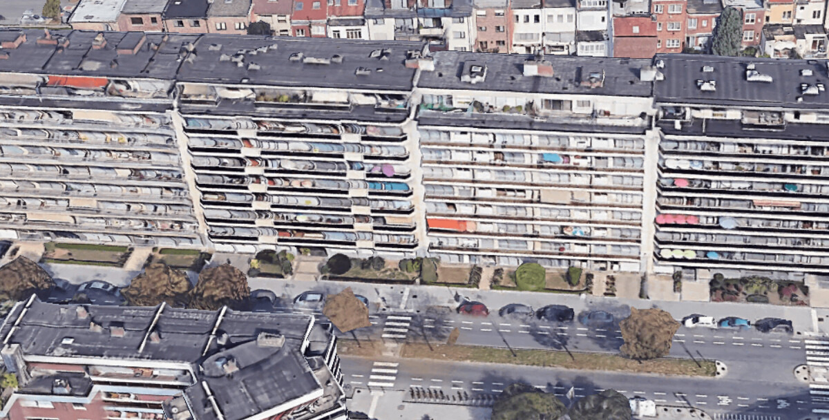 Vue aérienne d'un grand immeuble résidentiel avec balcons colorés, entouré de bâtiments et d'une route bordée d'arbres.