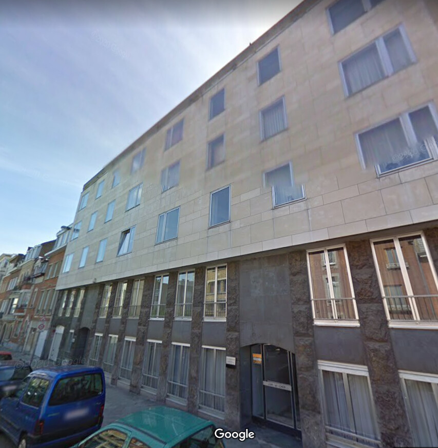 Bâtiment résidentiel beige à plusieurs étages avec des fenêtres rectangulaires, situé dans une rue urbaine avec des voitures garées.