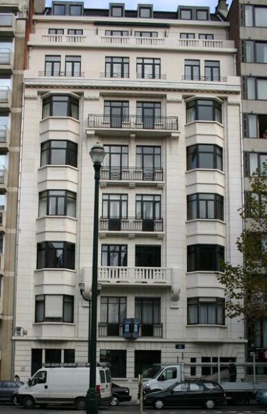 Façade d'un immeuble blanc à plusieurs étages avec balcons et fenêtres noires, situé sur l'avenue Louise à Bruxelles.