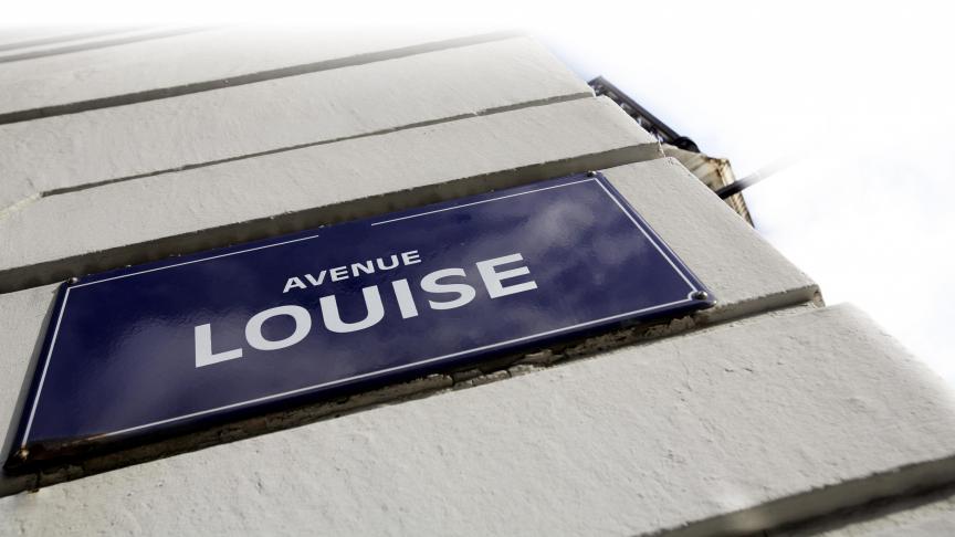 Plaque de rue bleue avec l'inscription "Avenue Louise" sur un mur en briques blanches.