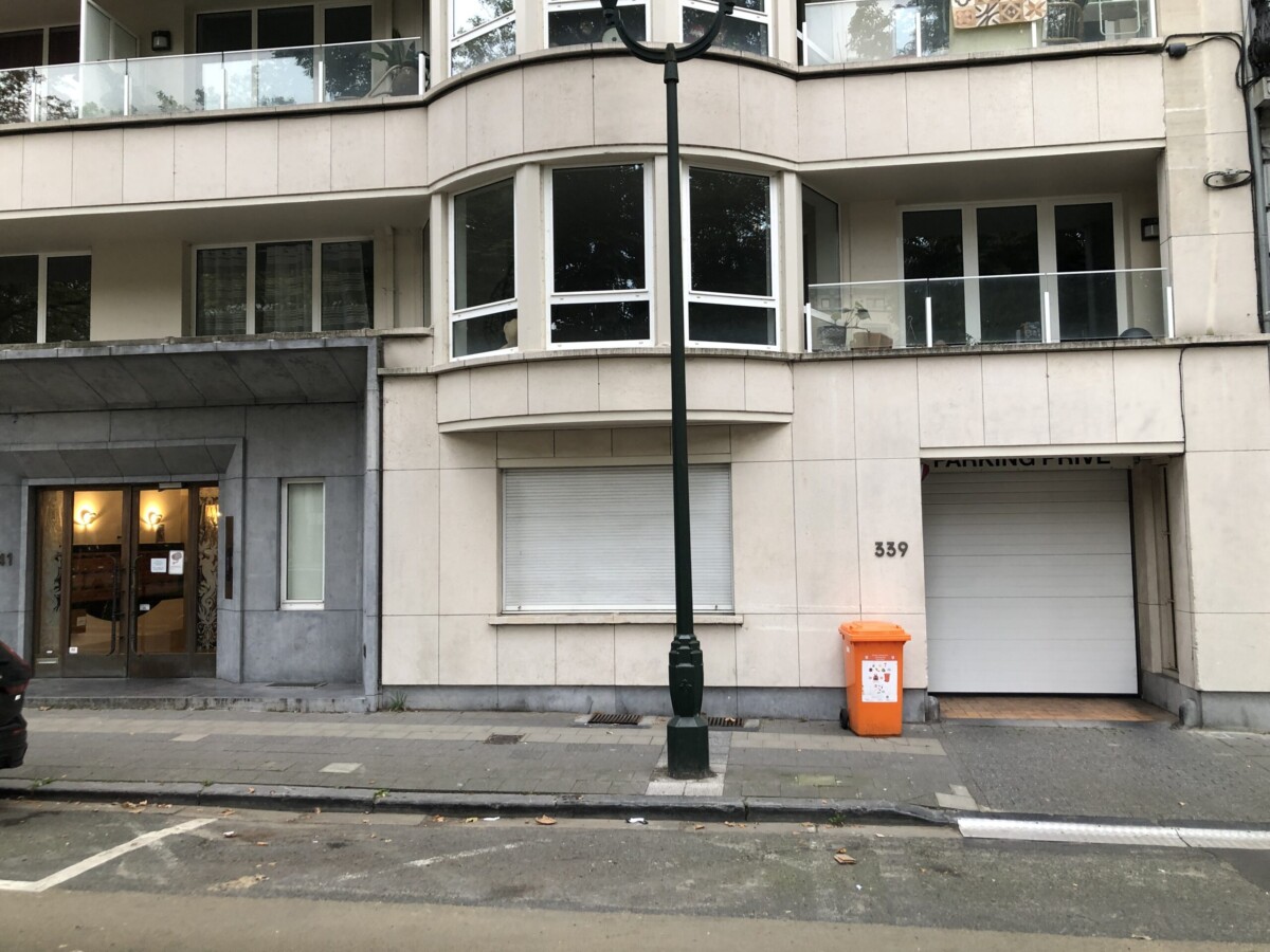 Façade d'un immeuble beige avec balcon vitré au 339, entrée à gauche et poubelle orange près du garage.