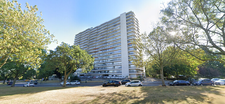 Immeuble résidentiel moderne et blanc entouré d'arbres avec des voitures garées devant, sous un ciel bleu dégagé.