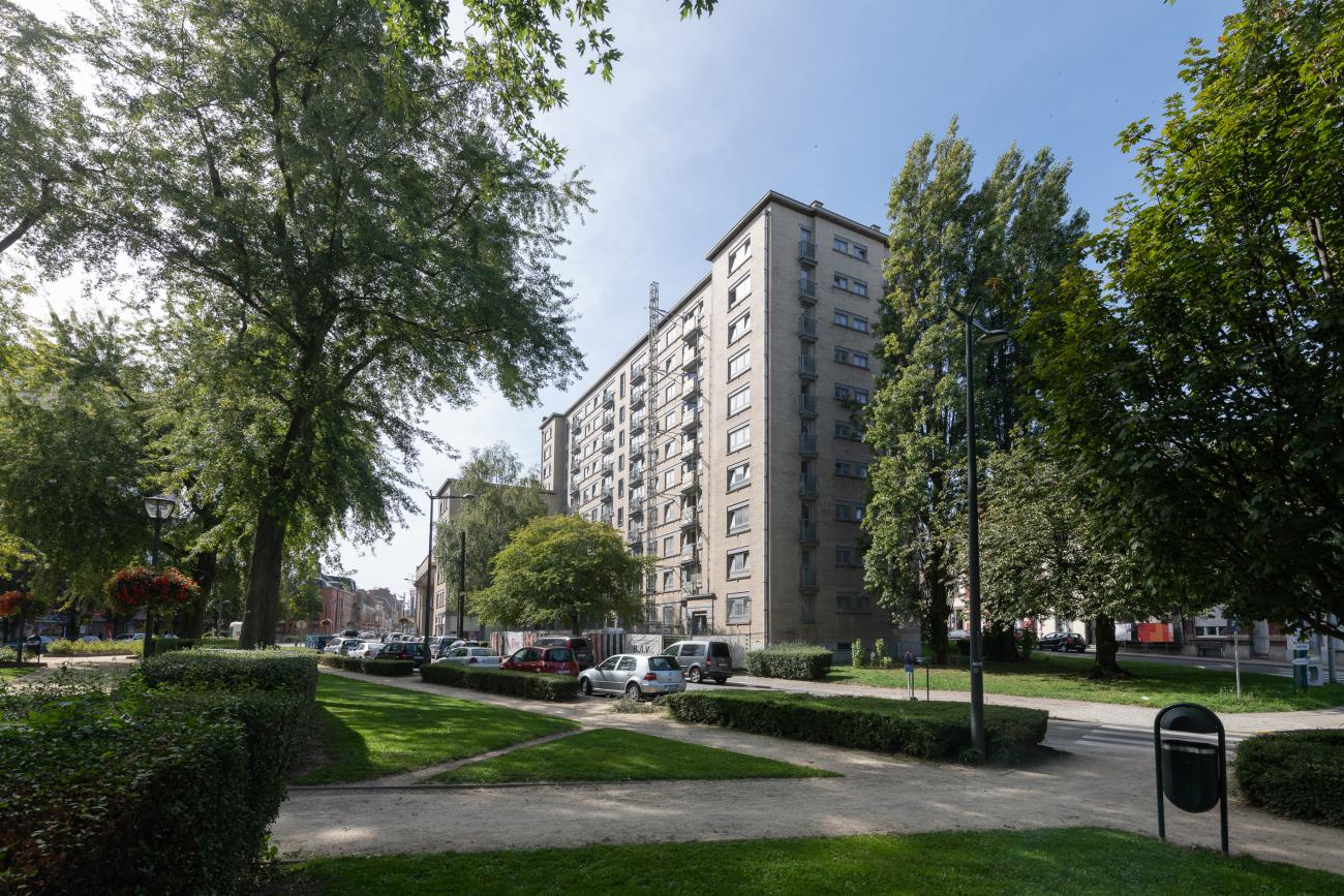 Immeuble résidentiel en briques, entouré d'arbres et de voitures stationnées, situé dans le square Albert sous un ciel bleu.