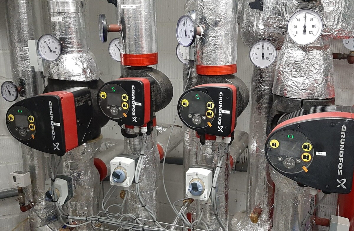 Trois pompes Grundfos rouges et noires sont fixées à des tuyaux isolés, avec plusieurs manomètres affichant des mesures.